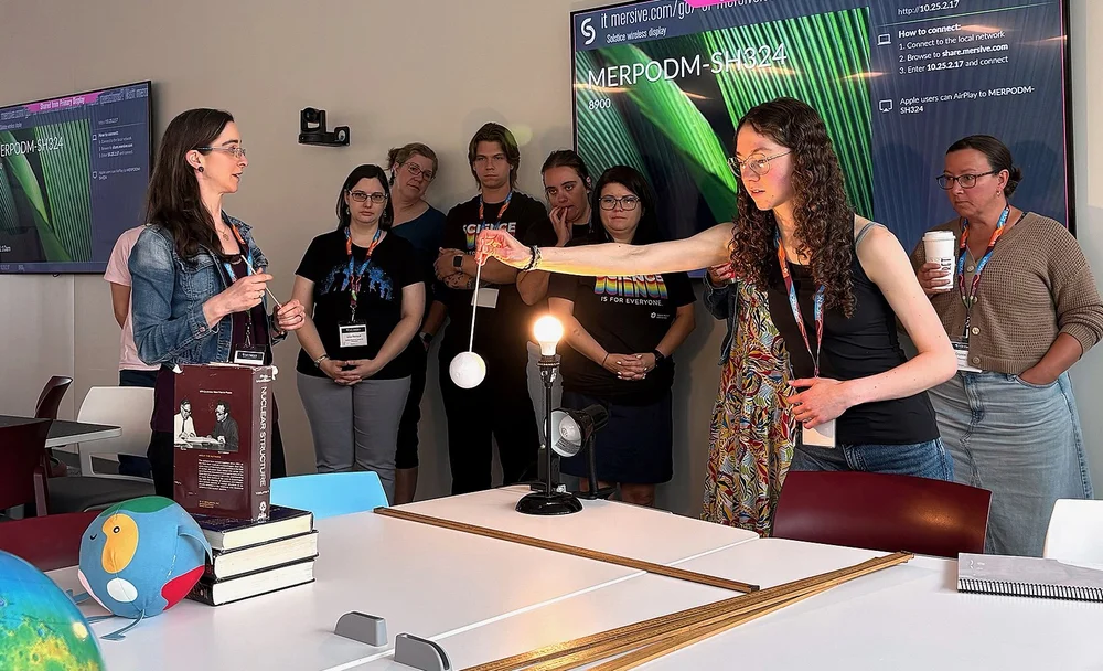 Person holding a Styrofoam ball  behind a light bulb with people standing watching