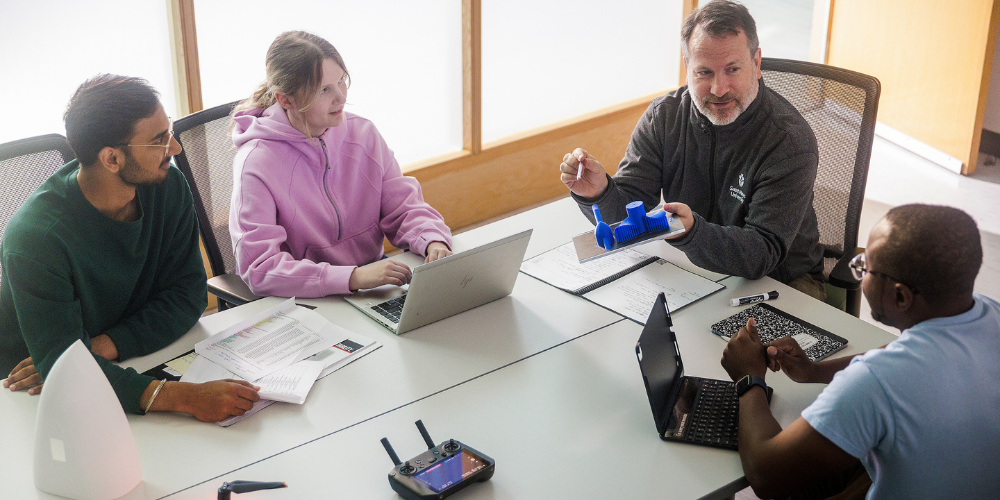 A professor sits and talks with engineering students
