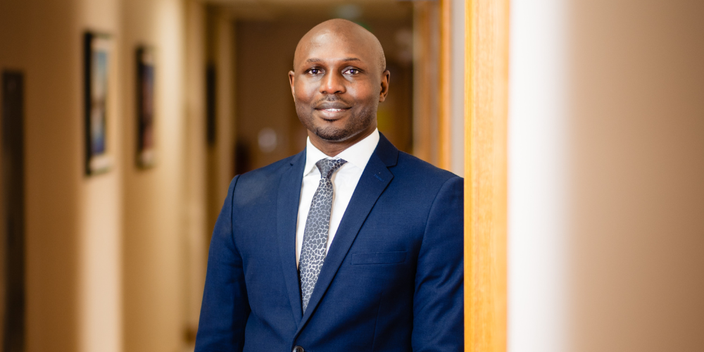 Ayo wears a navy suit and looks toward the camera