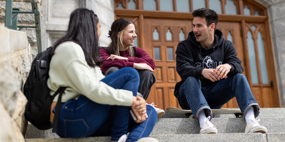 Three students sit on the front steps of the McNally building