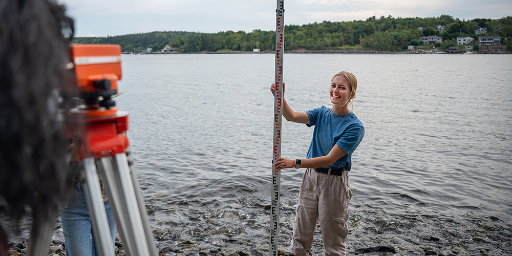 A student holds a measuring gauge while standing in the water.